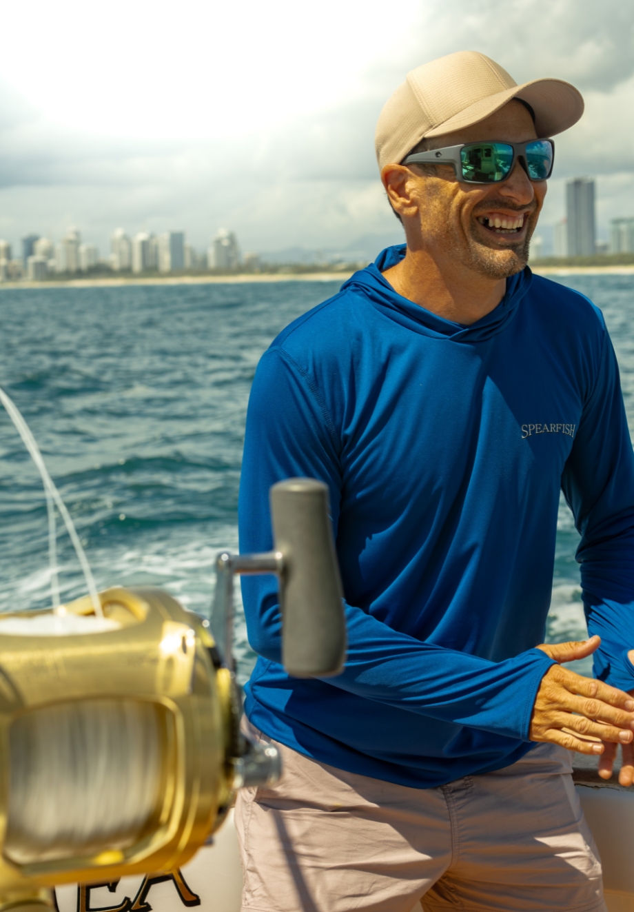 Angler wearing Mkaira custom fishing apparel on a boat featuring a premium blue gamefishing shirt designed for offshore fishing.